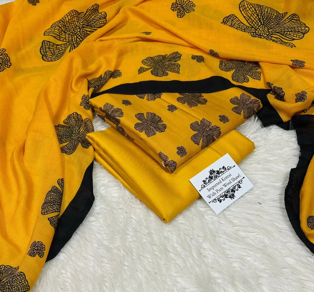Yellow wool shawl with black floral patterns and black border, folded on white textured background