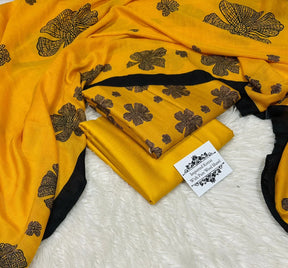 Yellow wool shawl with black floral patterns and black border, folded on white textured background