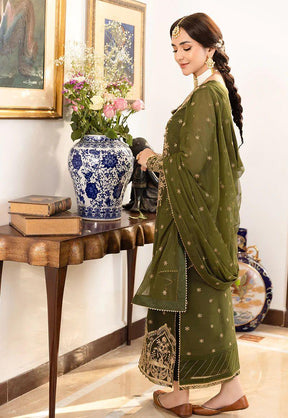 Woman in olive green embroidered traditional dress standing near table with blue floral vase and flowers