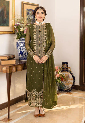 Woman wearing an olive green embroidered traditional outfit with floral patterns, standing indoors beside decorative vases and paintings